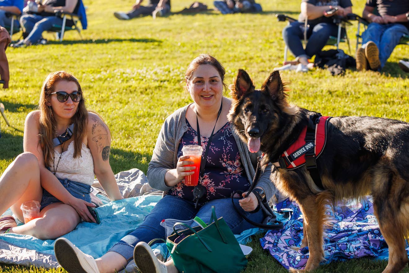 A woman sitting on a blanket in the lawn with her service dog.