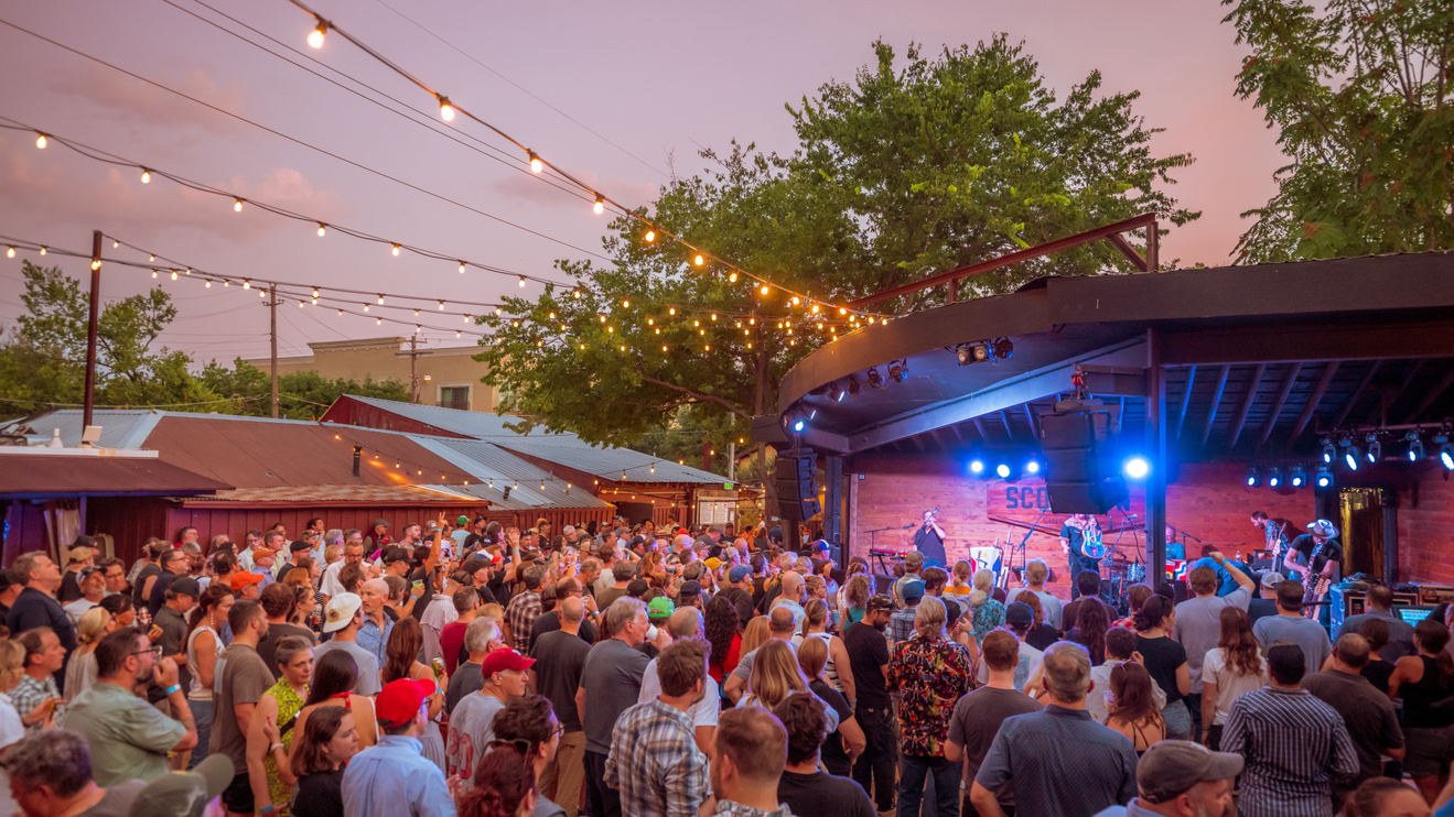 A crowd of people at an event at Scoot's Inn with string lights above the area