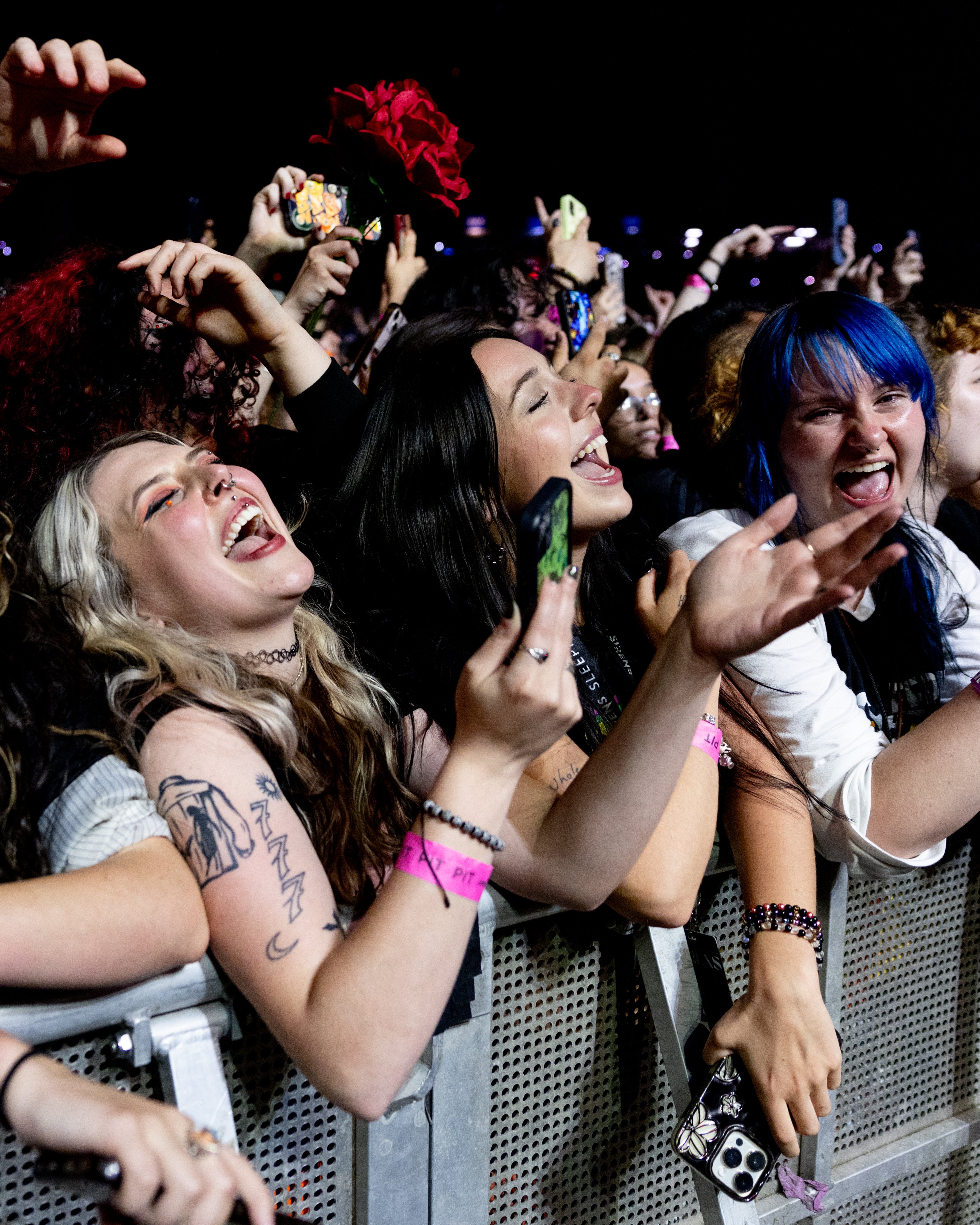 Three female fans on the rail singing and smiling while Pierce The Veil performs at PNC Music Pavilion.