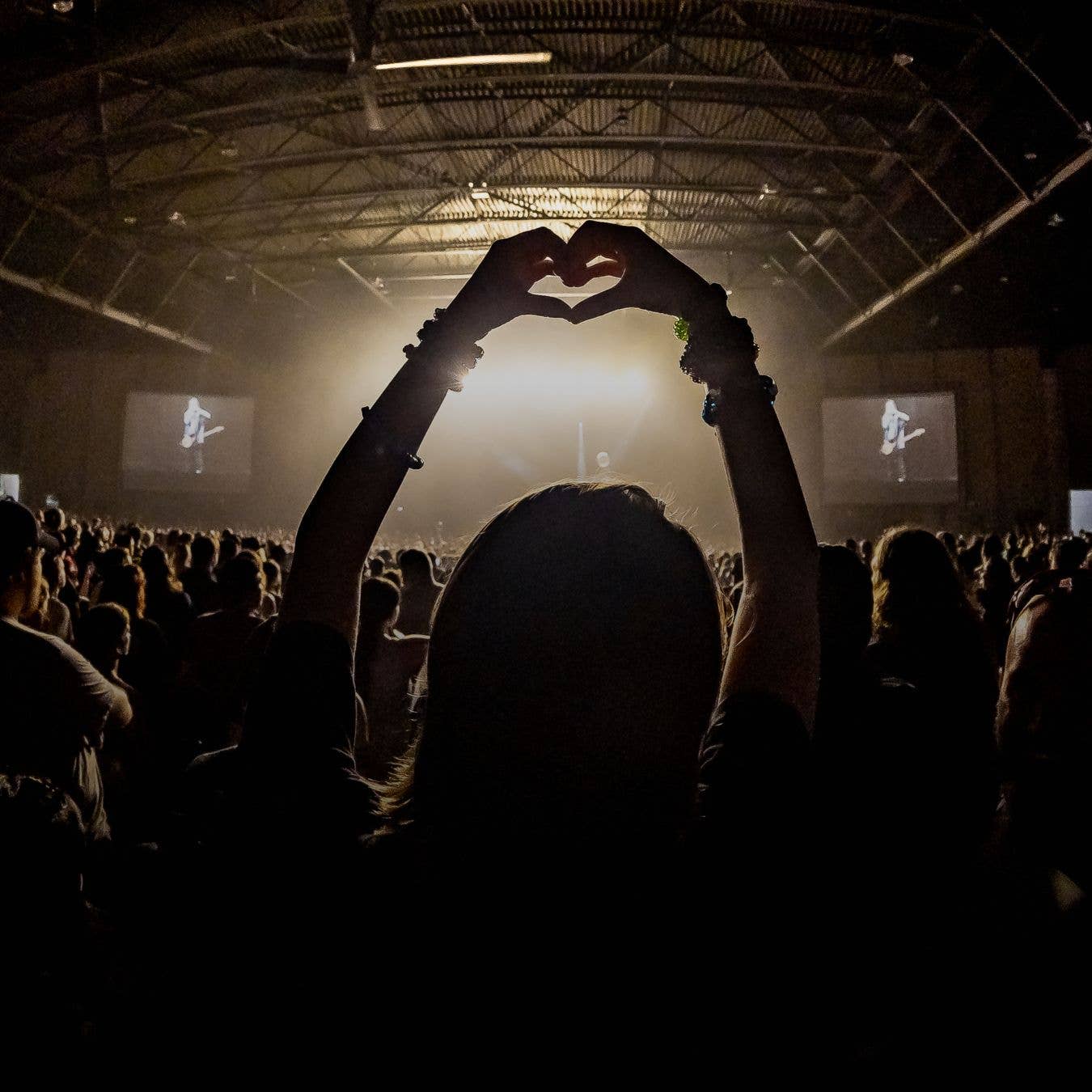 A silhouette photo of a fan making a heart with her hands while watching a show
