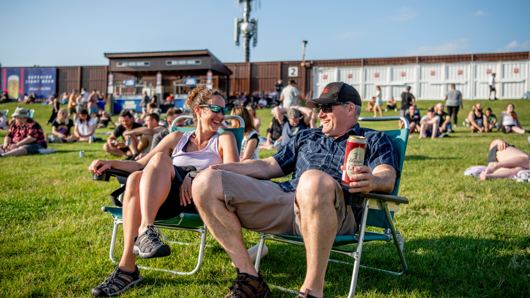 2 fans sitting in rental Lawn chairs on the Lawn, laughing with one another.