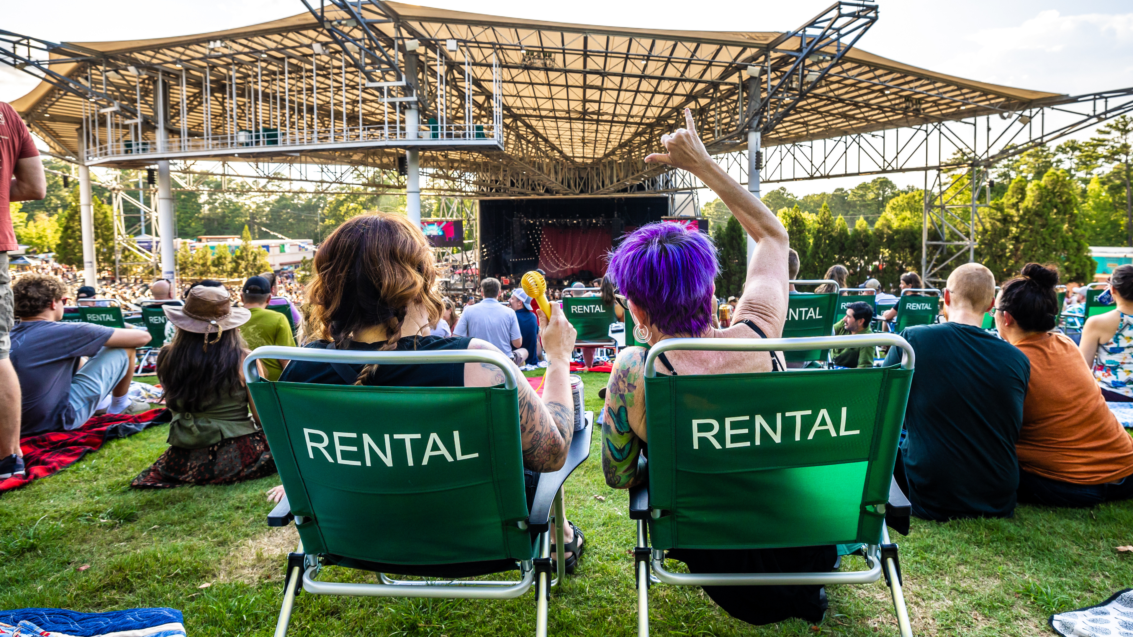 Concert attendees seated in green rental lawn chairs on a grassy lawn, watching and enjoying a live concert.