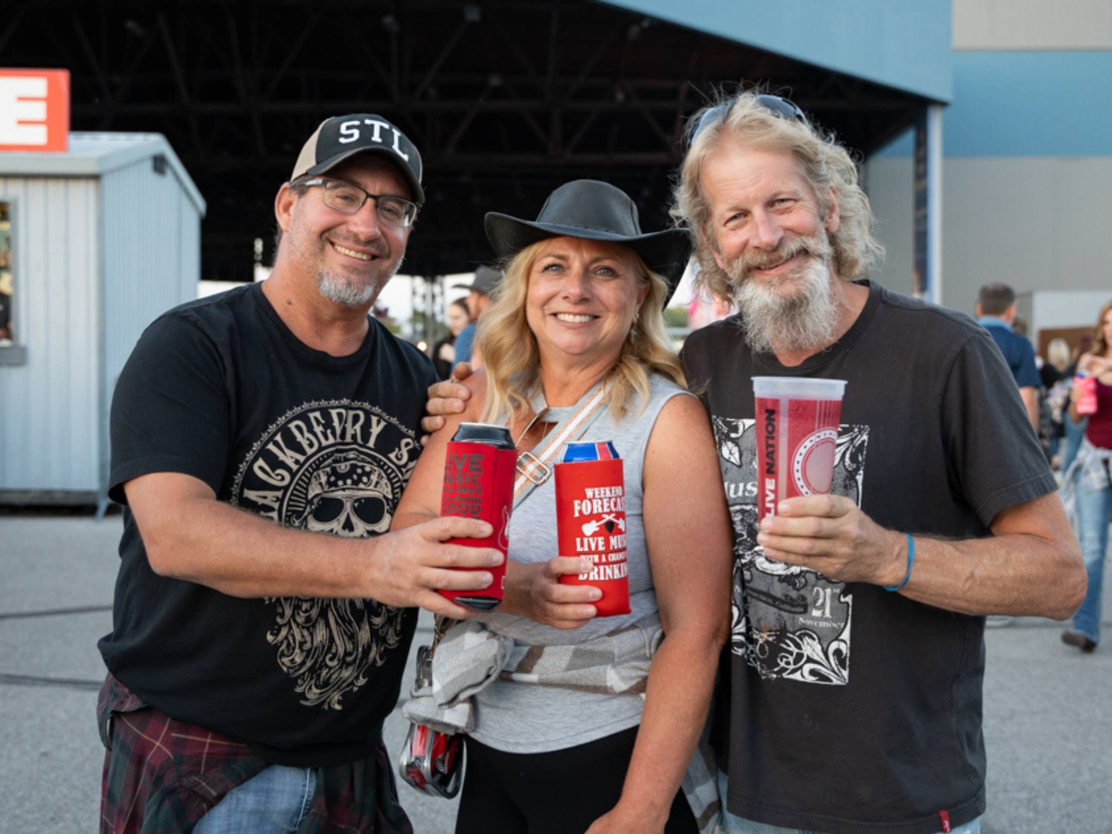 Three people posing and smiling at the camera while holding drinks.