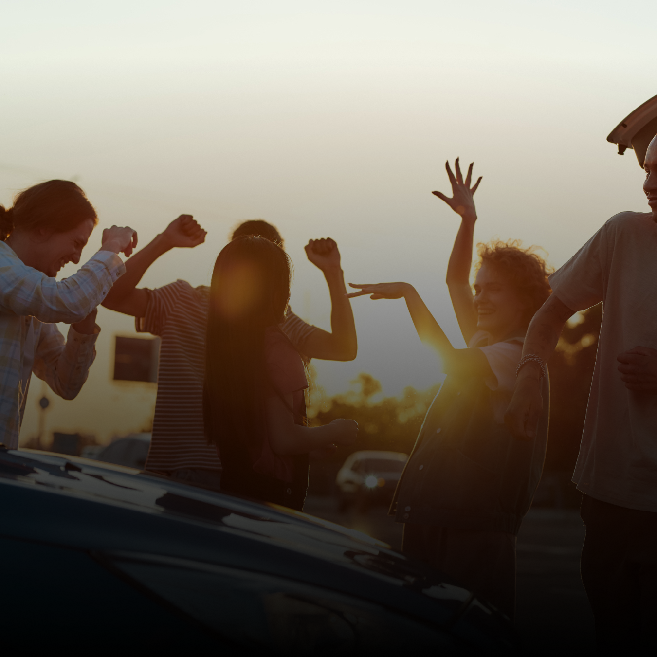 a group of friends dancing around a car 