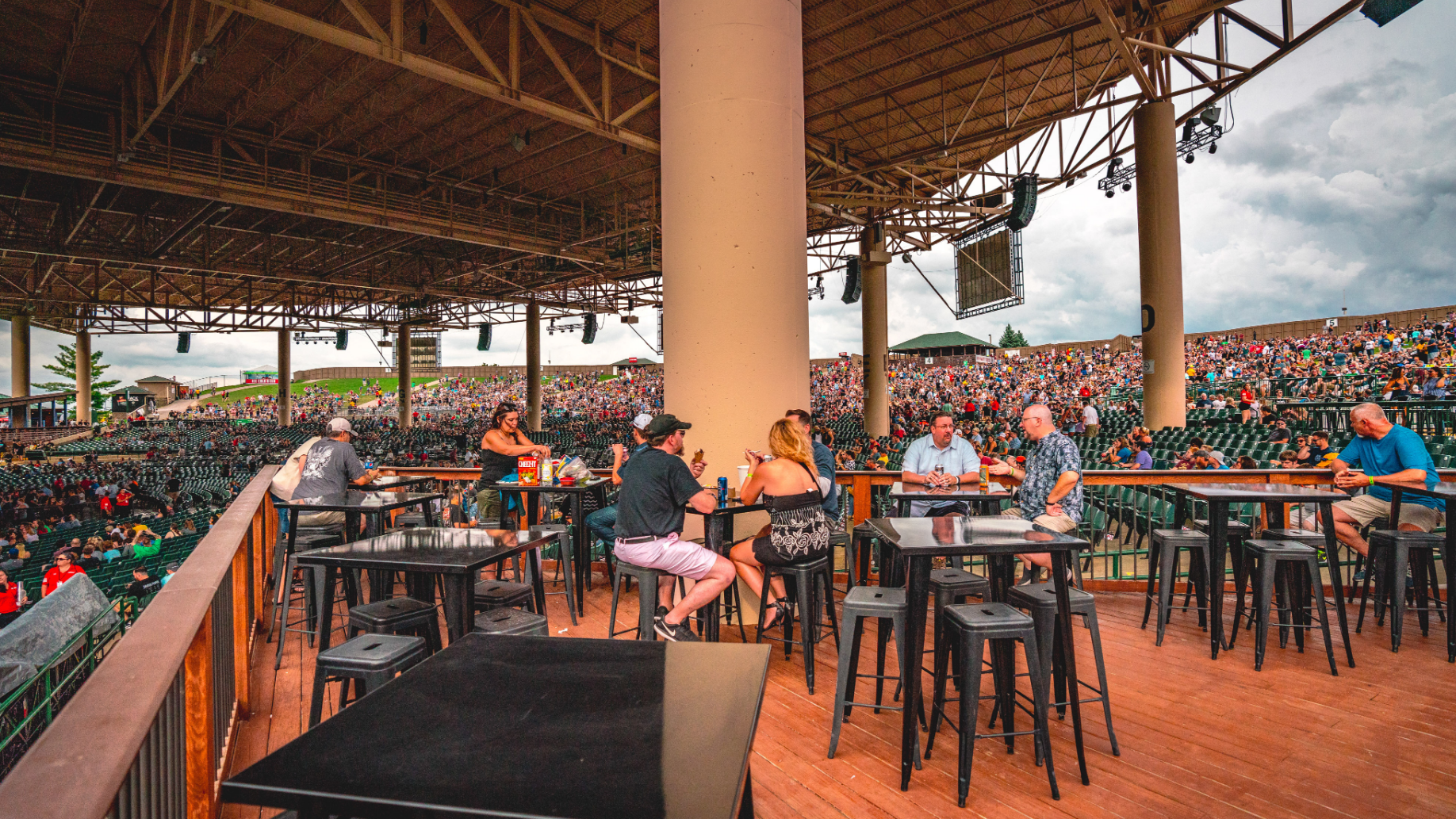 Fans sitting around high-top tables with food and drinks, overlooking the concourse to the side of the stage. 