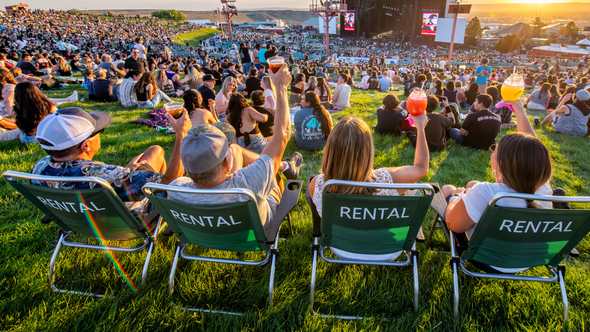 Four friends cheers their drinks while sitting in lawn chairs and watching the show.