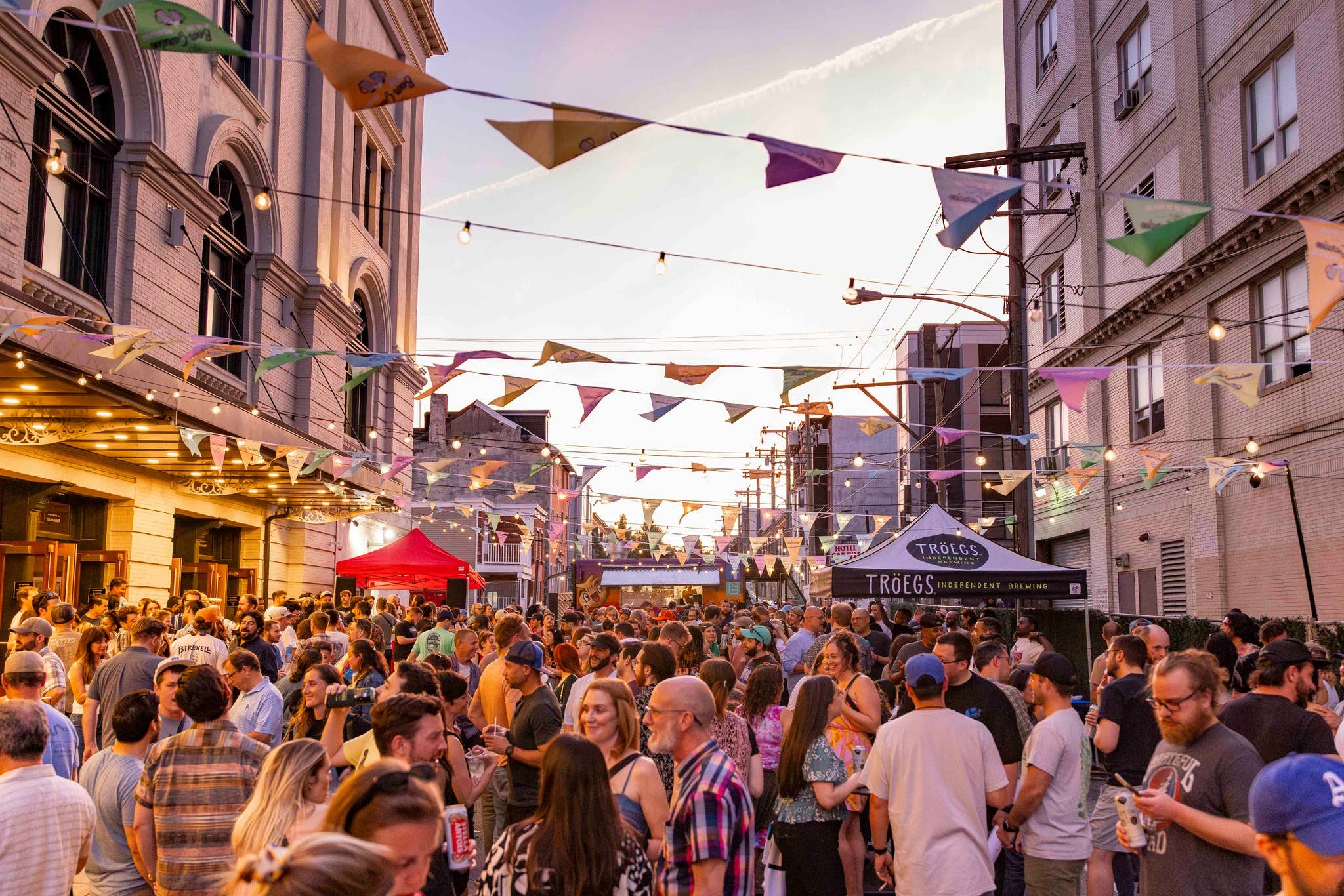 A crowd of people walking underneath the banners and string lights