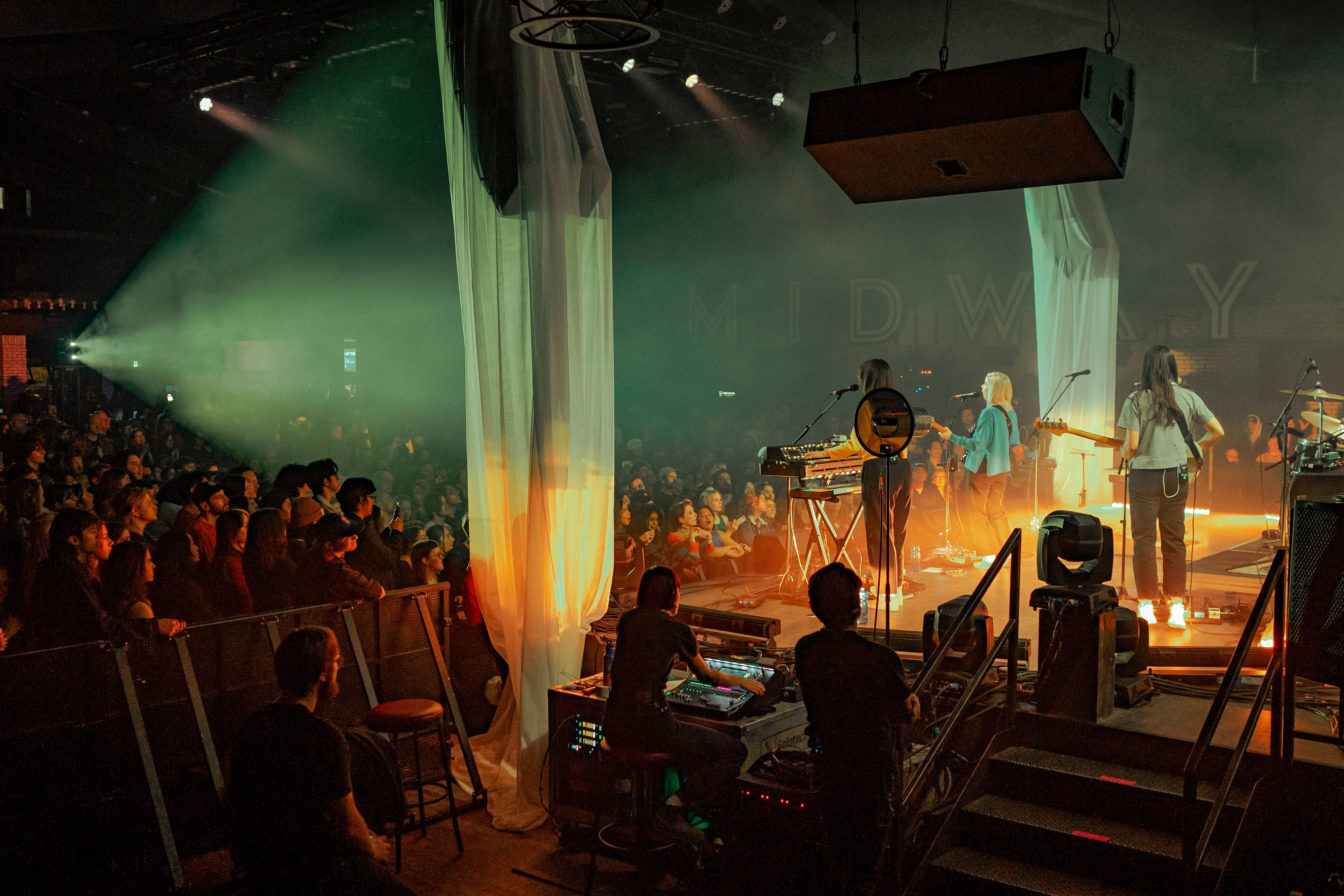 view of the stage at  midway music hall from behind looking onto the backs of band on stage and the crowd