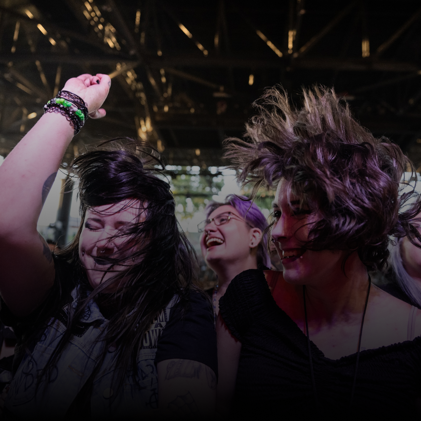 Three young fans dancing in the crowd with their hair flying around and their hand in the air