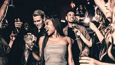 A group of people smiling and dancing in a crowd with drinks in their hands