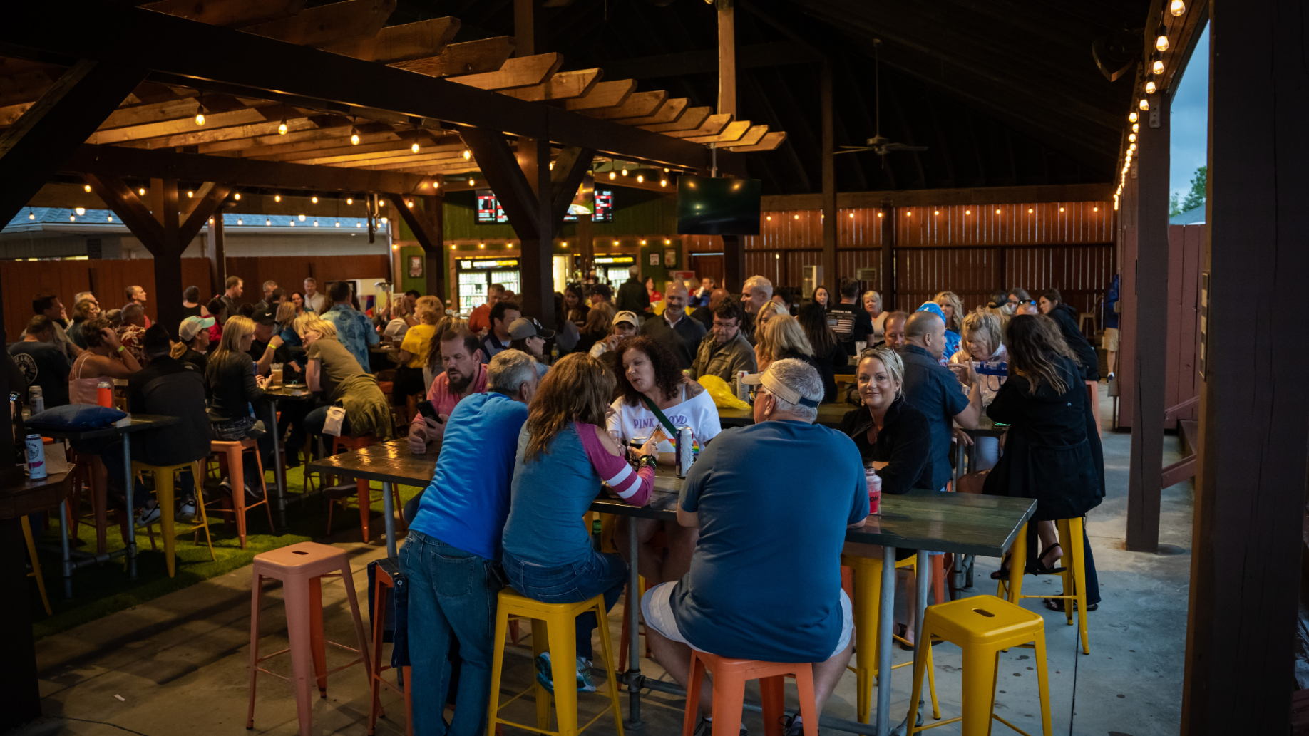 Multiple fans sitting around high-top tables while eating, drinking, and mingling with one another. Twinkling lights line the roof. 