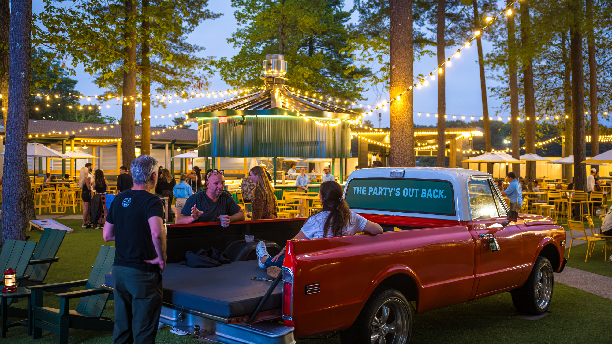 Fans sit in the back of a pick-up truck chatting and having drinks.