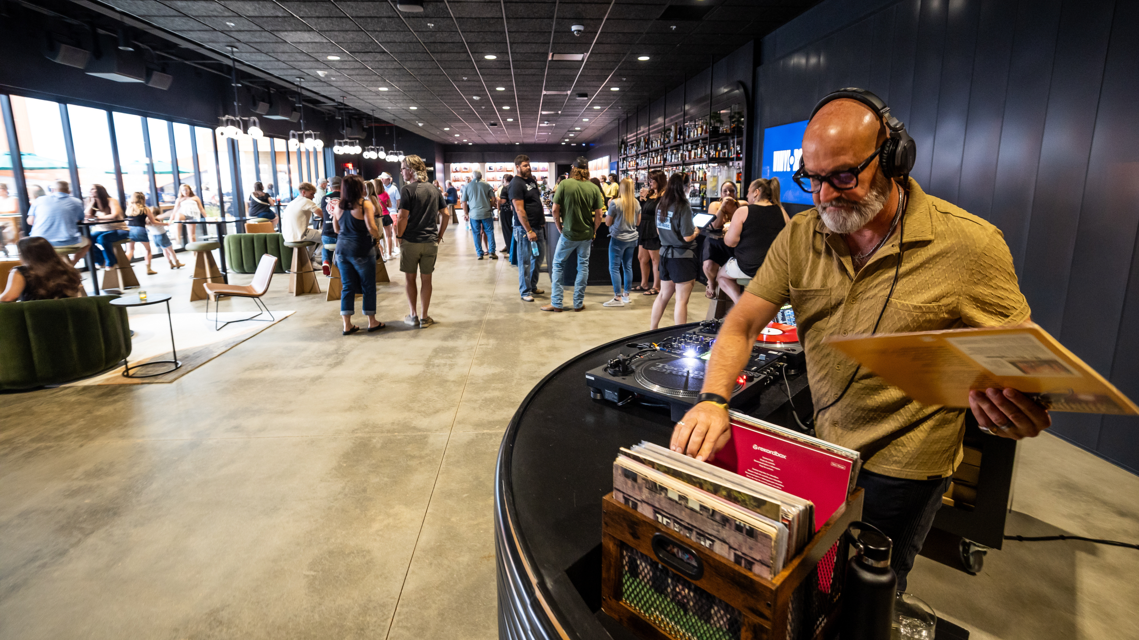 A DJ plays records in a modern indoor lounge while guests gather, socialize, and enjoy drinks before an event.