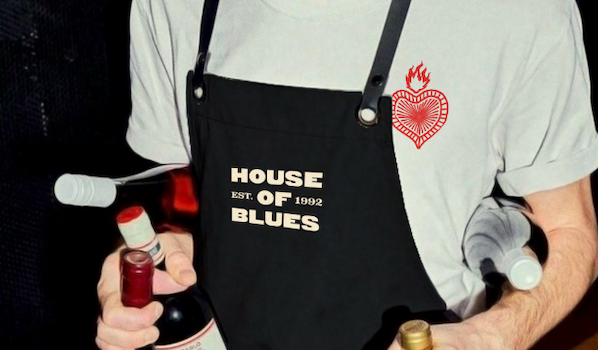 A person wearing a House of Blues tee shirt and apron holding bottles