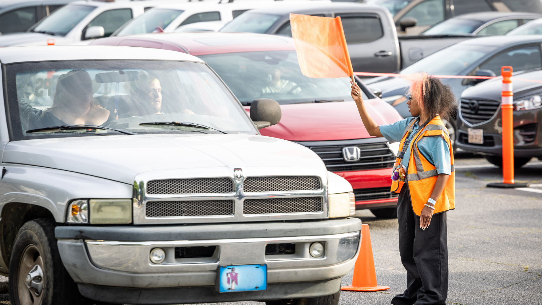 An employee holding an orange flag directing car traffic inside of a parking lot. 