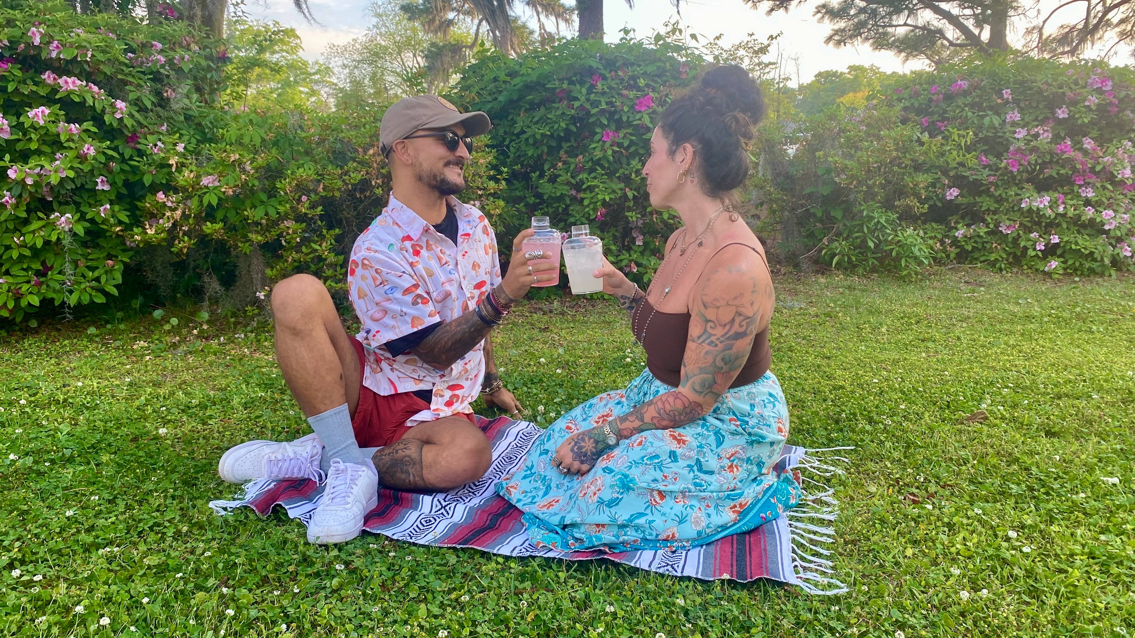 A man and woman sitting on a blanket in the grass with drinks at the show.