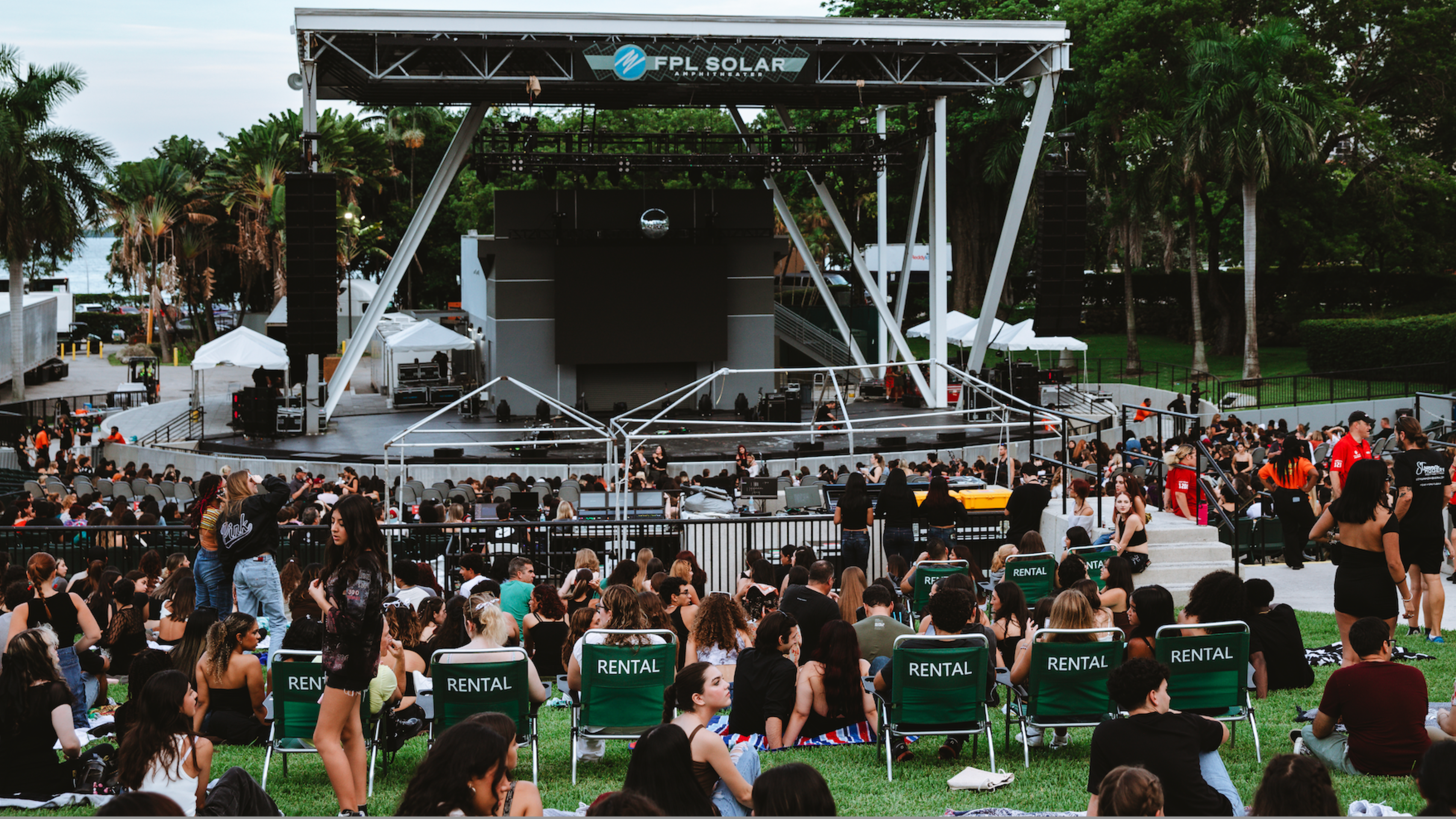 Concertgoers relax in green rental chairs facing the stage at FPL Solar Amphitheater during a show with the word “Paraíso” lit on the screen.