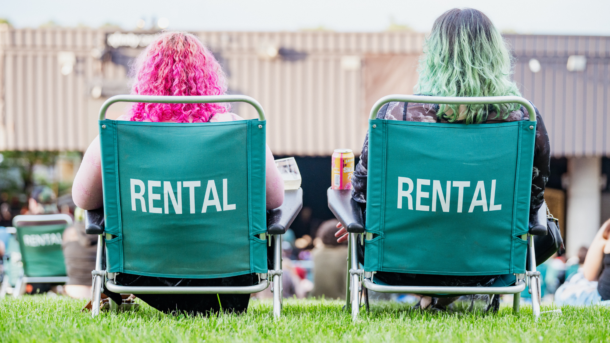 Two rental chairs on the lawn. Two women with colorful hair sit in them.
