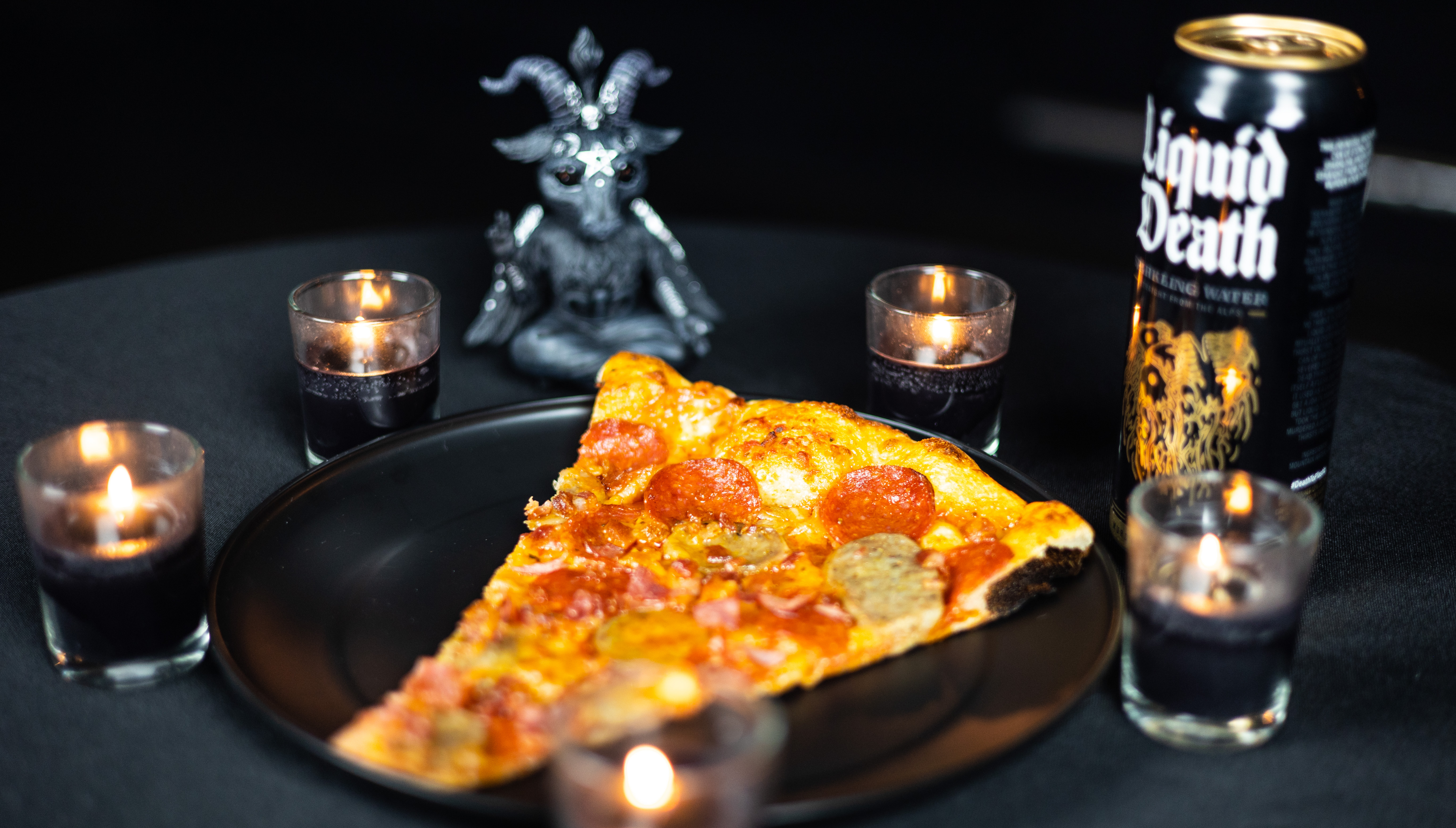 A slice of pizza surrounded by candles and a Liquid Death can