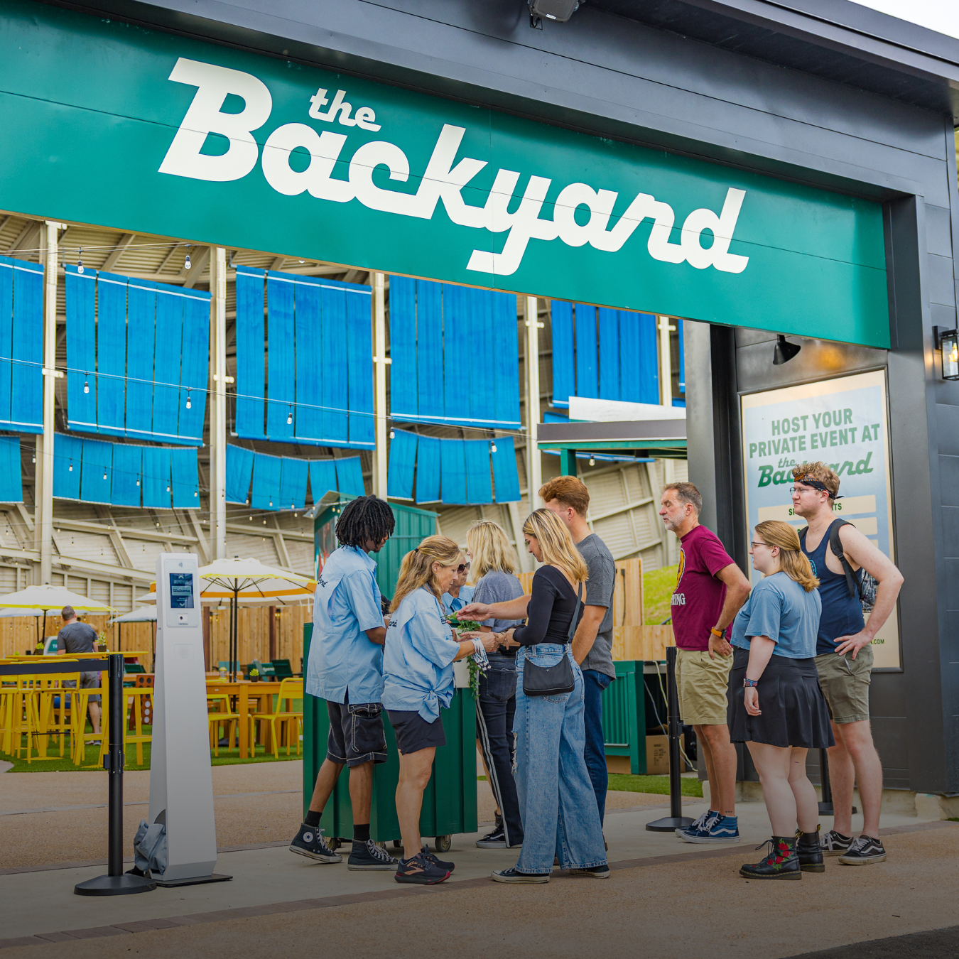 Guests entering The Backyard hospitality area, checking in with staff beneath a large entrance sign