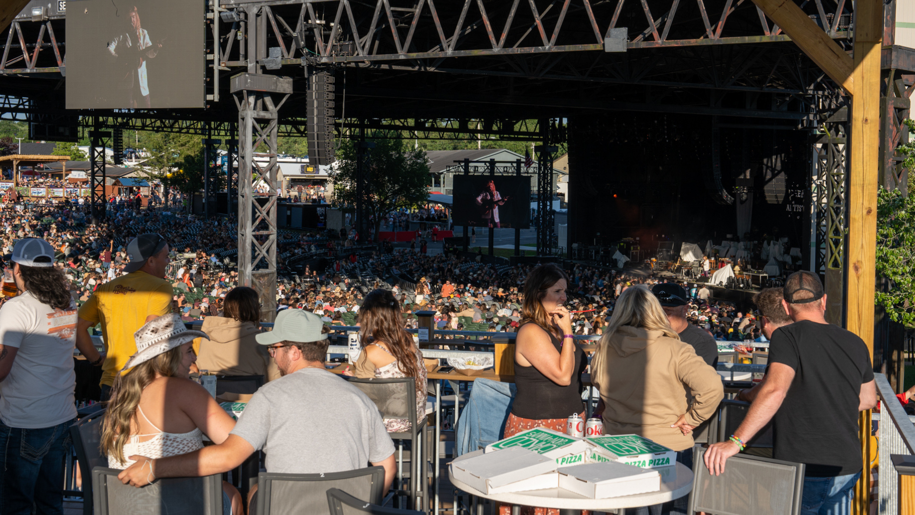 Fans sitting, standing, and chatting on the Lawn Party Deck. A view of the concourse and stage in the background. 
