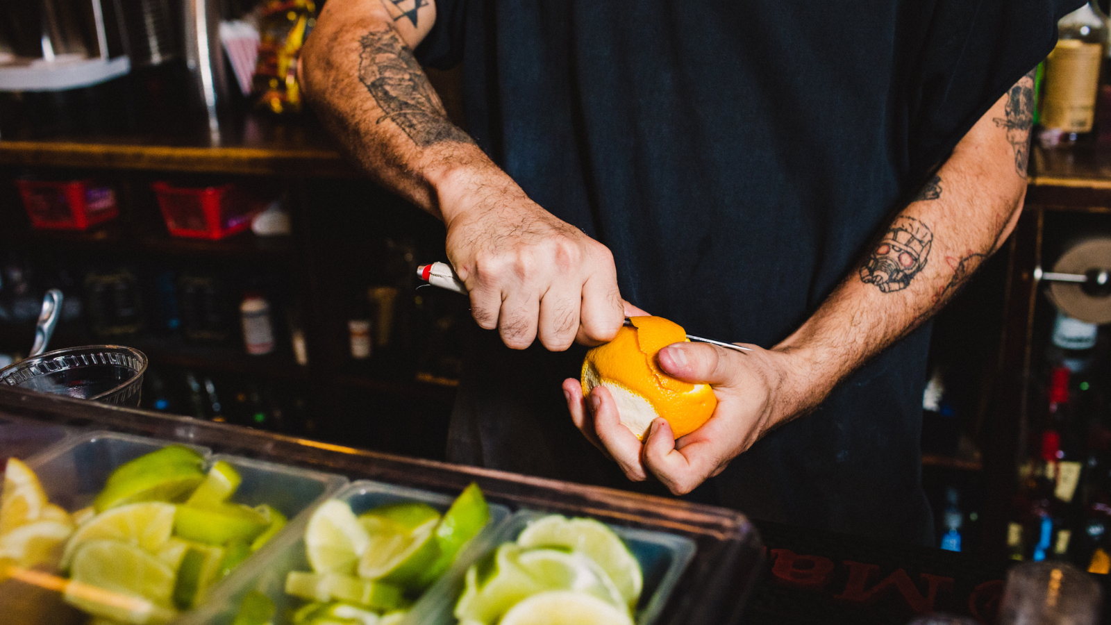 A close-up of a bartender peeling a fruit peel for a drink.