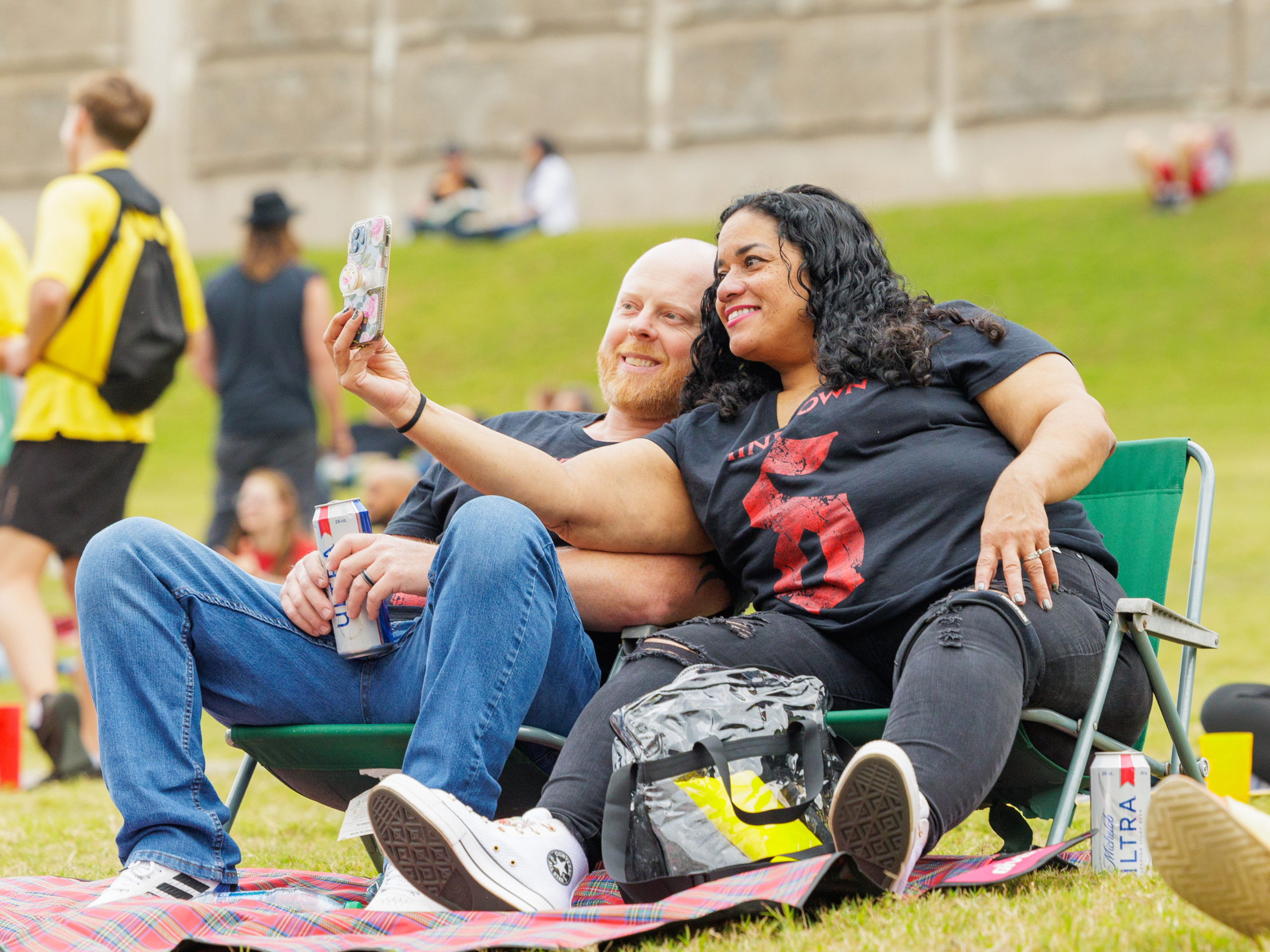A couple, sitting in lawn chair rentals, taking a selfie on the lawn.