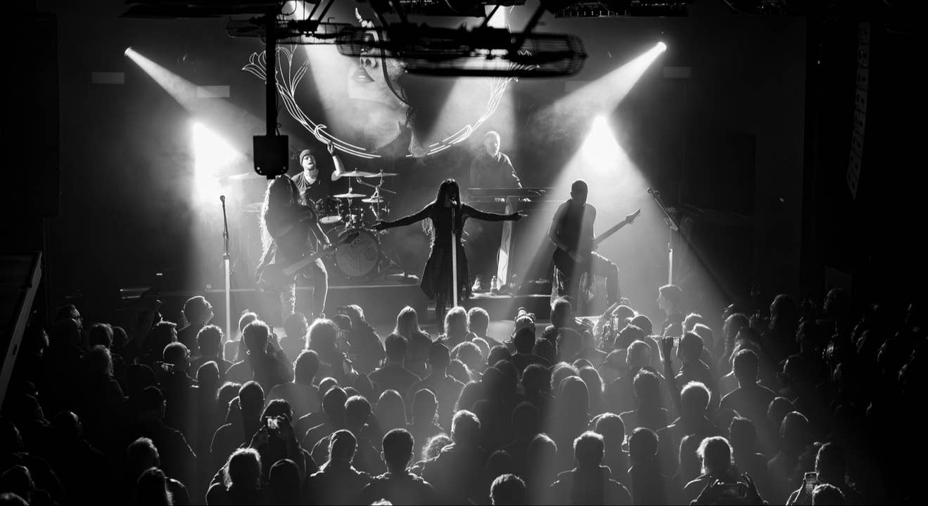 Black and white image of Artist on stage at The Mod Club in Toronto singing into a microphone with arms raised in the air