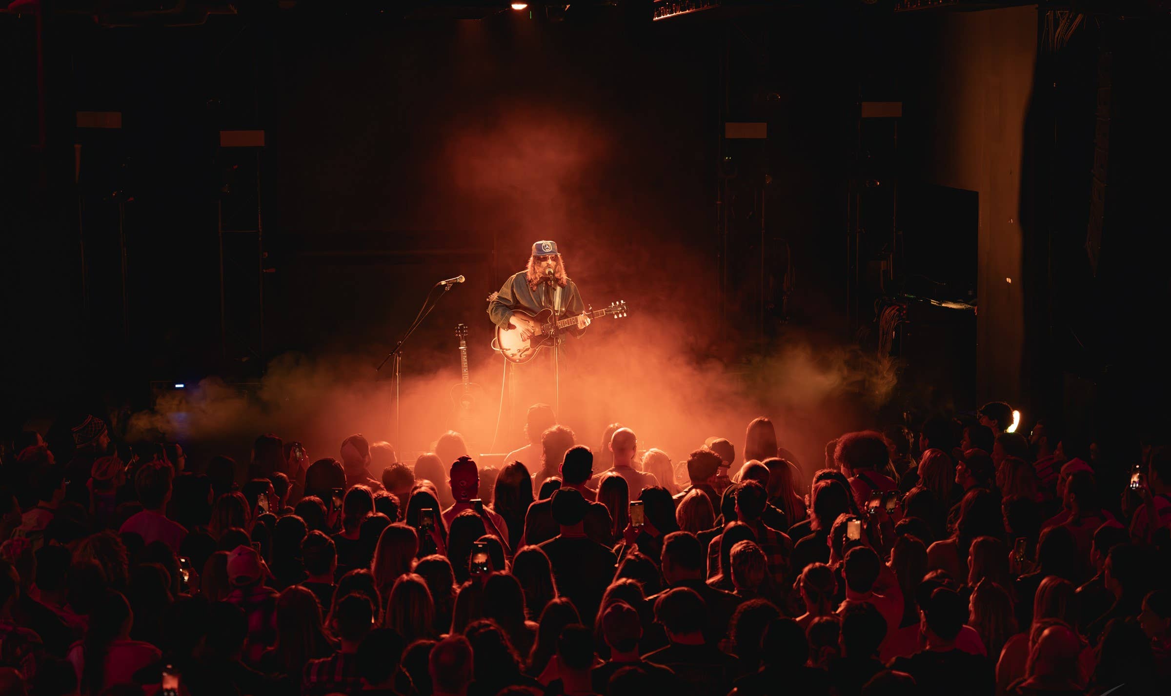 Artist with sunglasses on-stage singing into a crowd - orange fog covers the stage