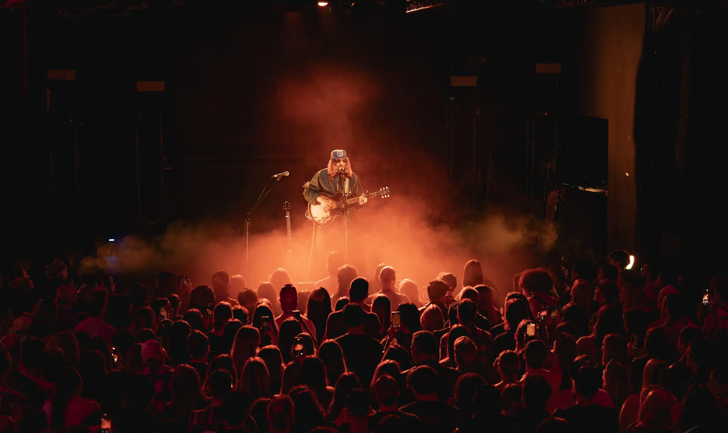 Artist with sunglasses on-stage singing into a crowd - orange fog covers the stage