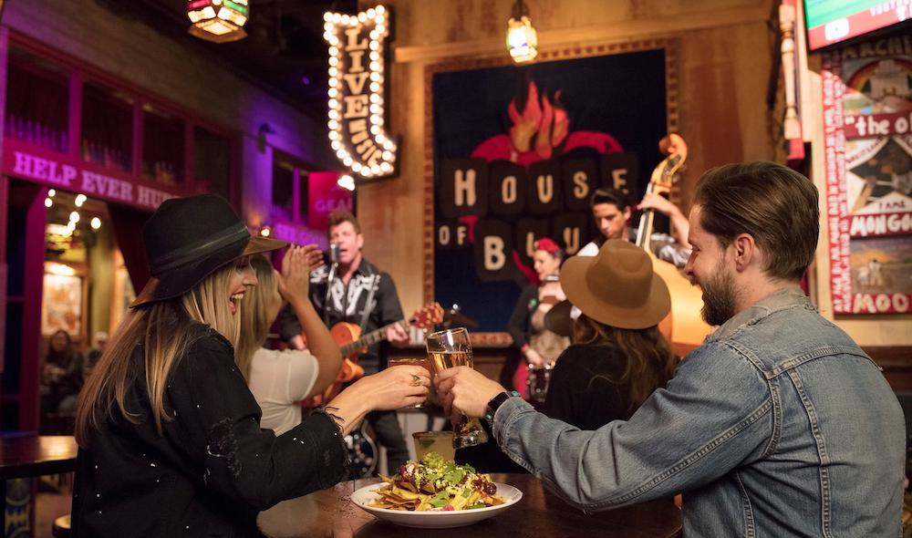 Two people cheers while sitting at a table facing a House of Blues stage