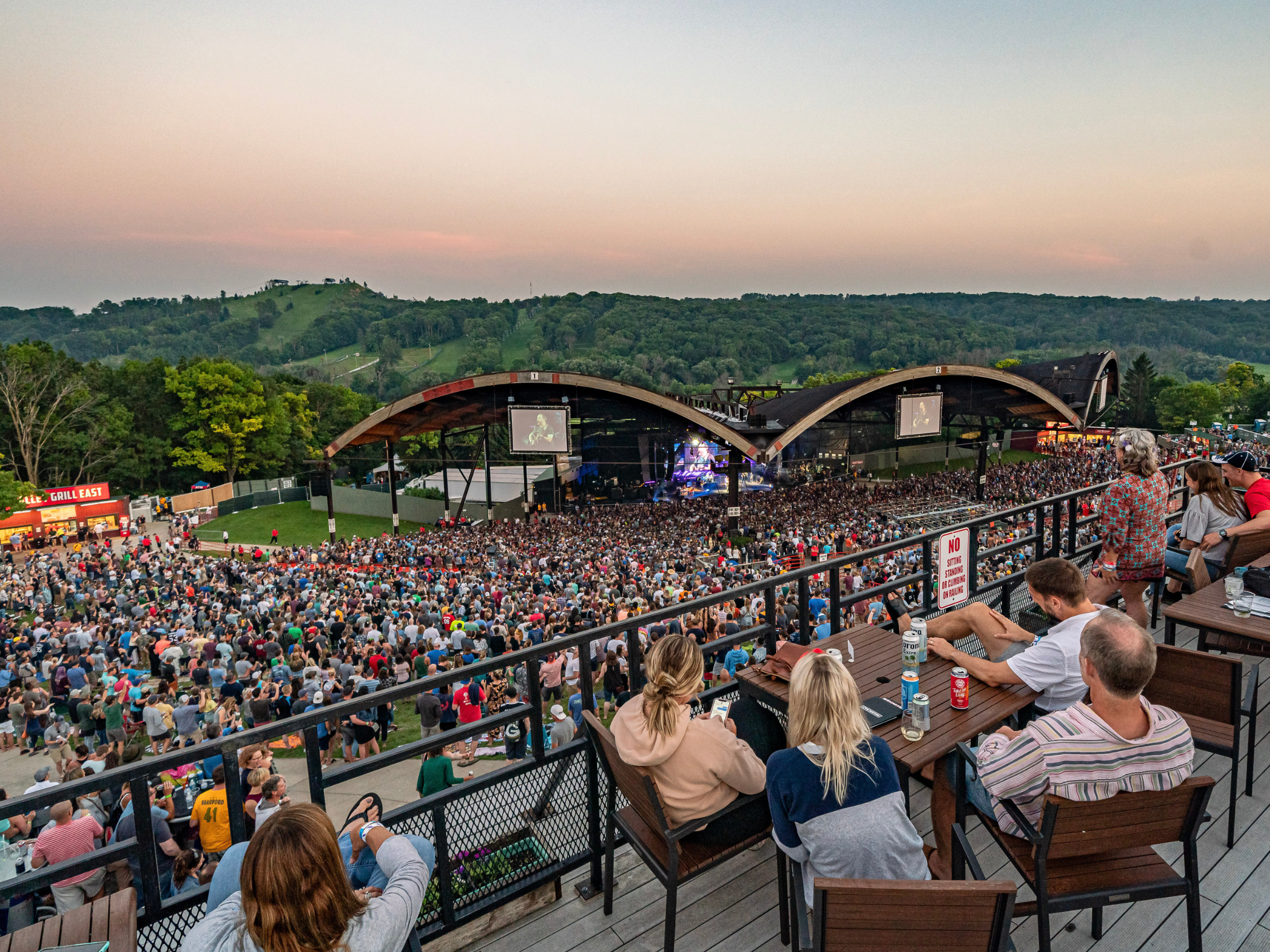 People sitting in chairs overlooking a crowd and the stage at Alpine Valley Music Theatre