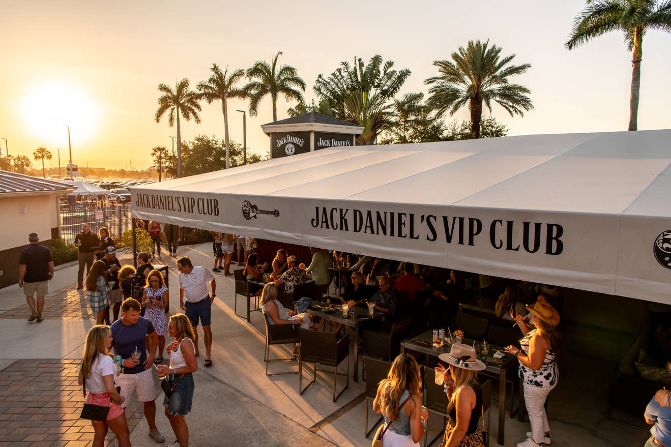 People spending time in the VIP Club section. There are tables and chairs under an awning. 