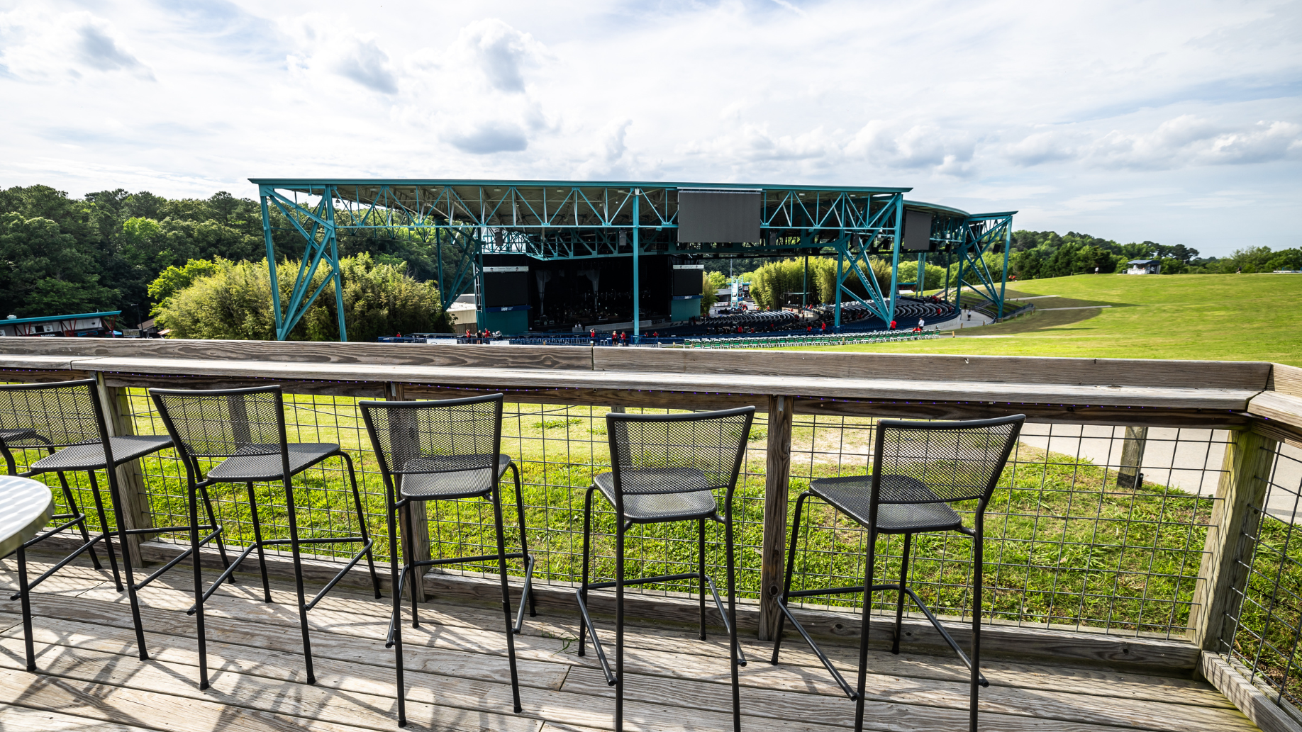 High-top bar stools on a fenced-off deck at the top of the lawn facing the stage.