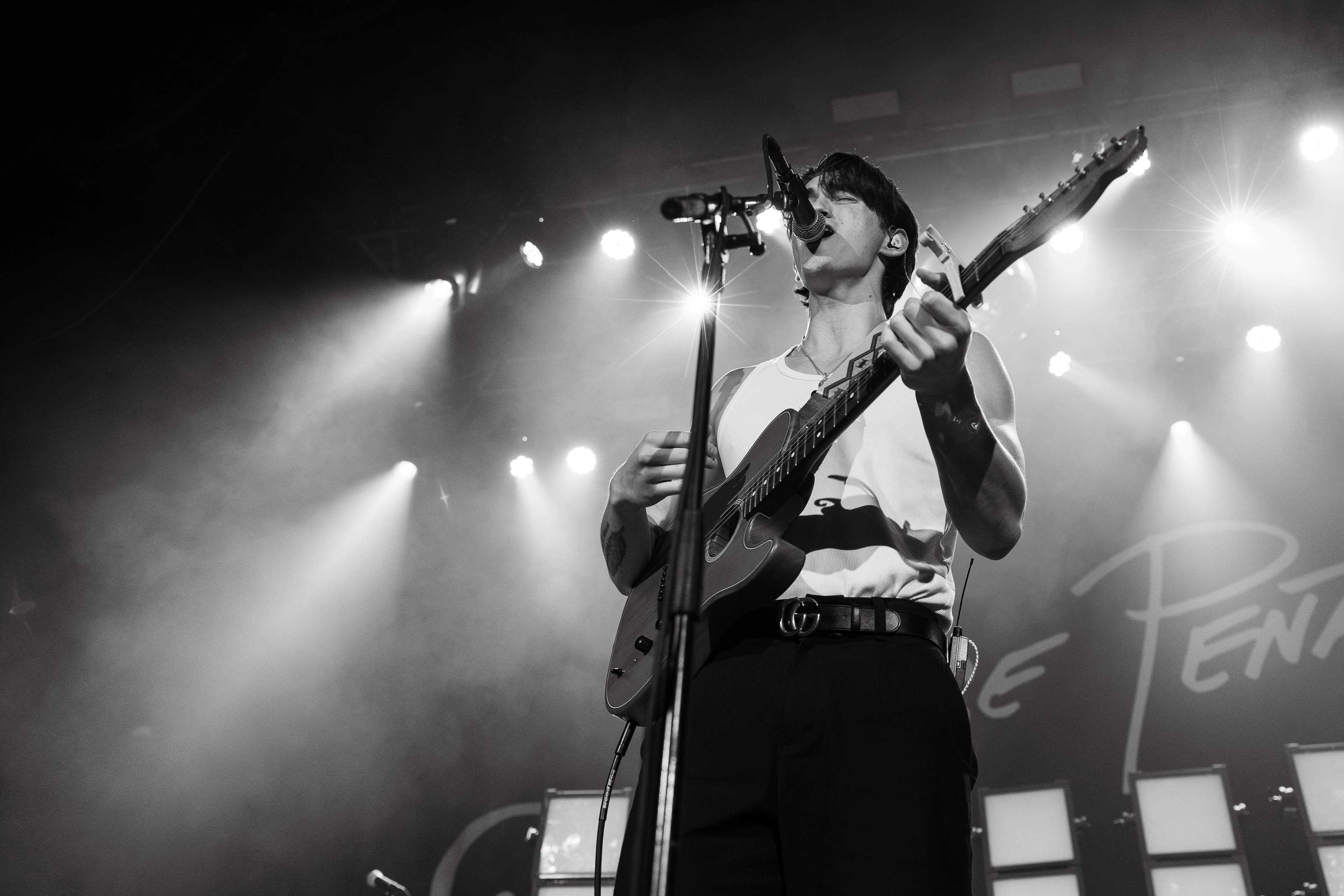 A man on stage singing and playing the guitar in black and white