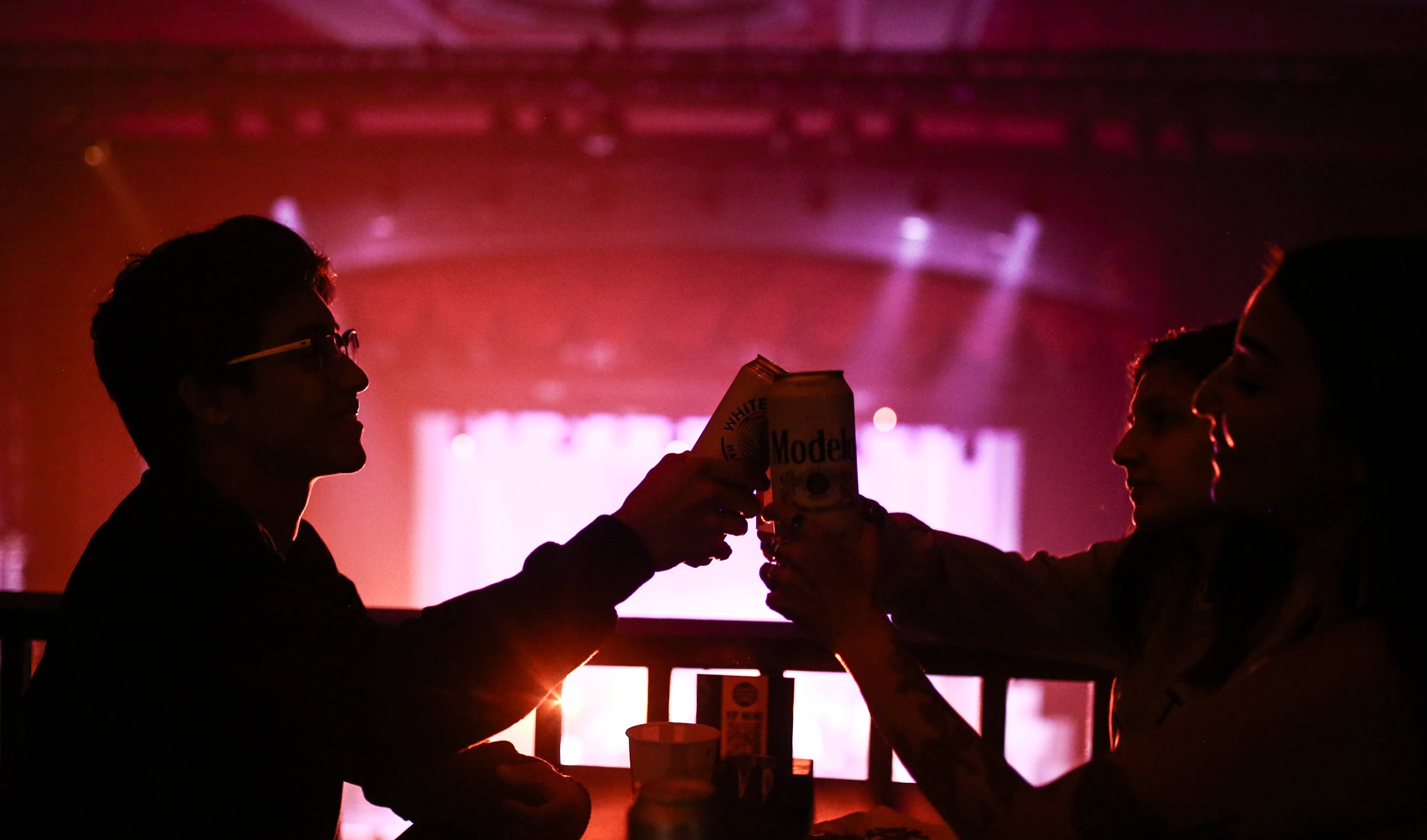 Two people holding cans cheersing each other while at an event