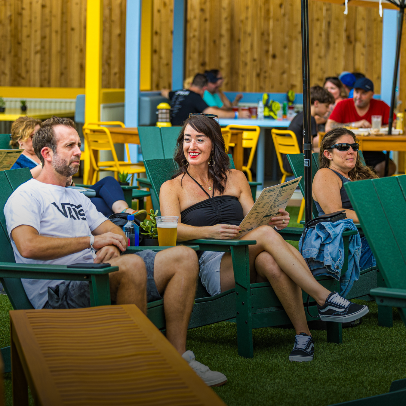 Guests seated in Adirondack chairs in The Backyard, holding beverages and menus
