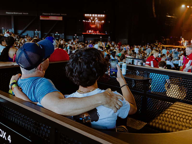 Two people with their arms around each other in the box seat area watching an event on stage