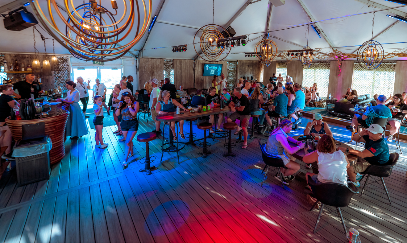 Many people sit at high top tables with drinks under the white tent of the Dominion Lounge.