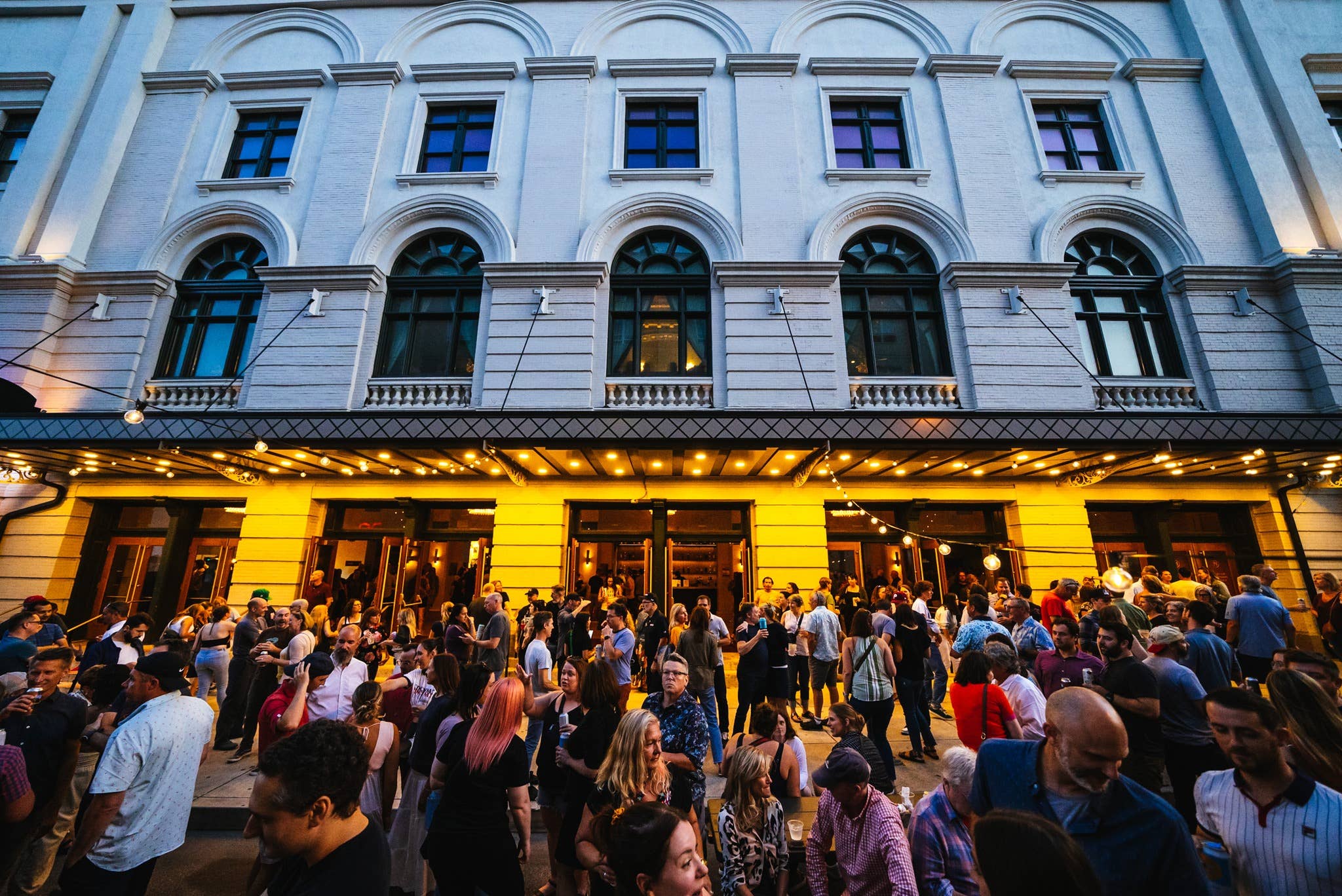 A close up image of the venue's main entrance before a show begins (a crowd of people standing outside with string lights displayed along the roof)