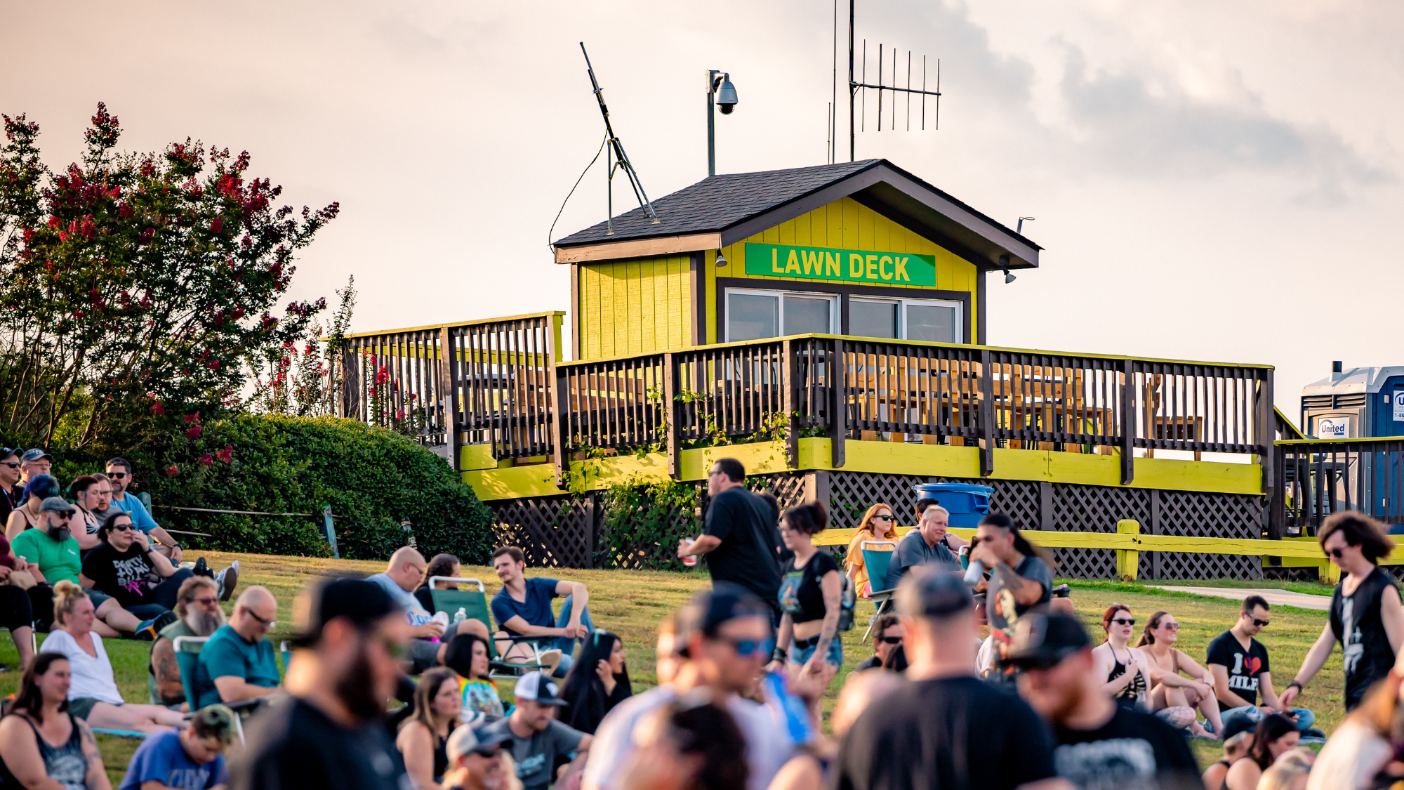 A deck at the back of the lawn overlooking the lawn. People sit in the lawn in front of it.