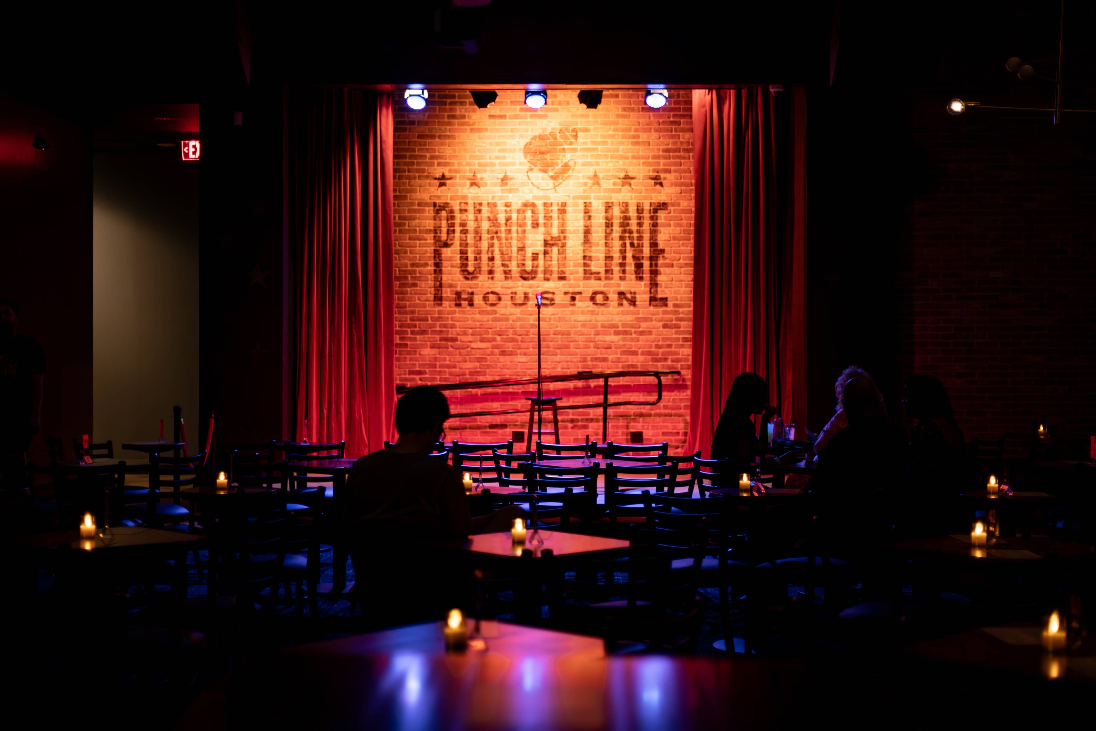 A few people sitting in the audience facing the stage with a brick background