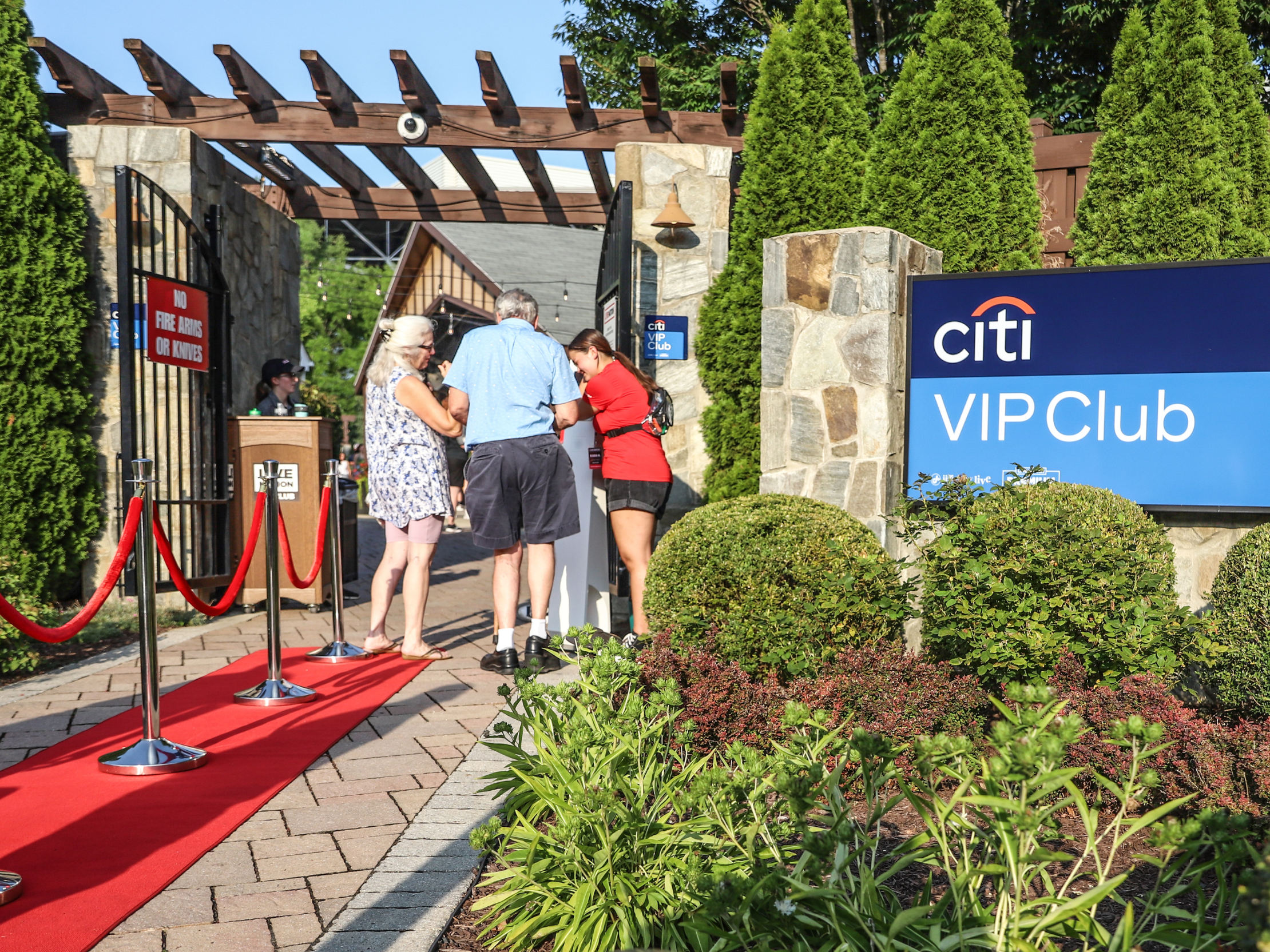 A pair of fans walking down a red carpet to enter the outdoor VIP Club.