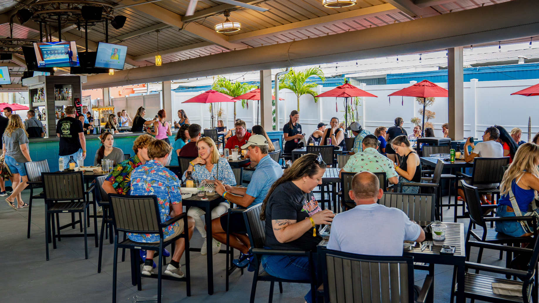 Fans sit at multiple tables eating, drinking, and chatting. Private bar in the background and television screens hanging from the ceiling, with some lights strung across the edges of the roof.