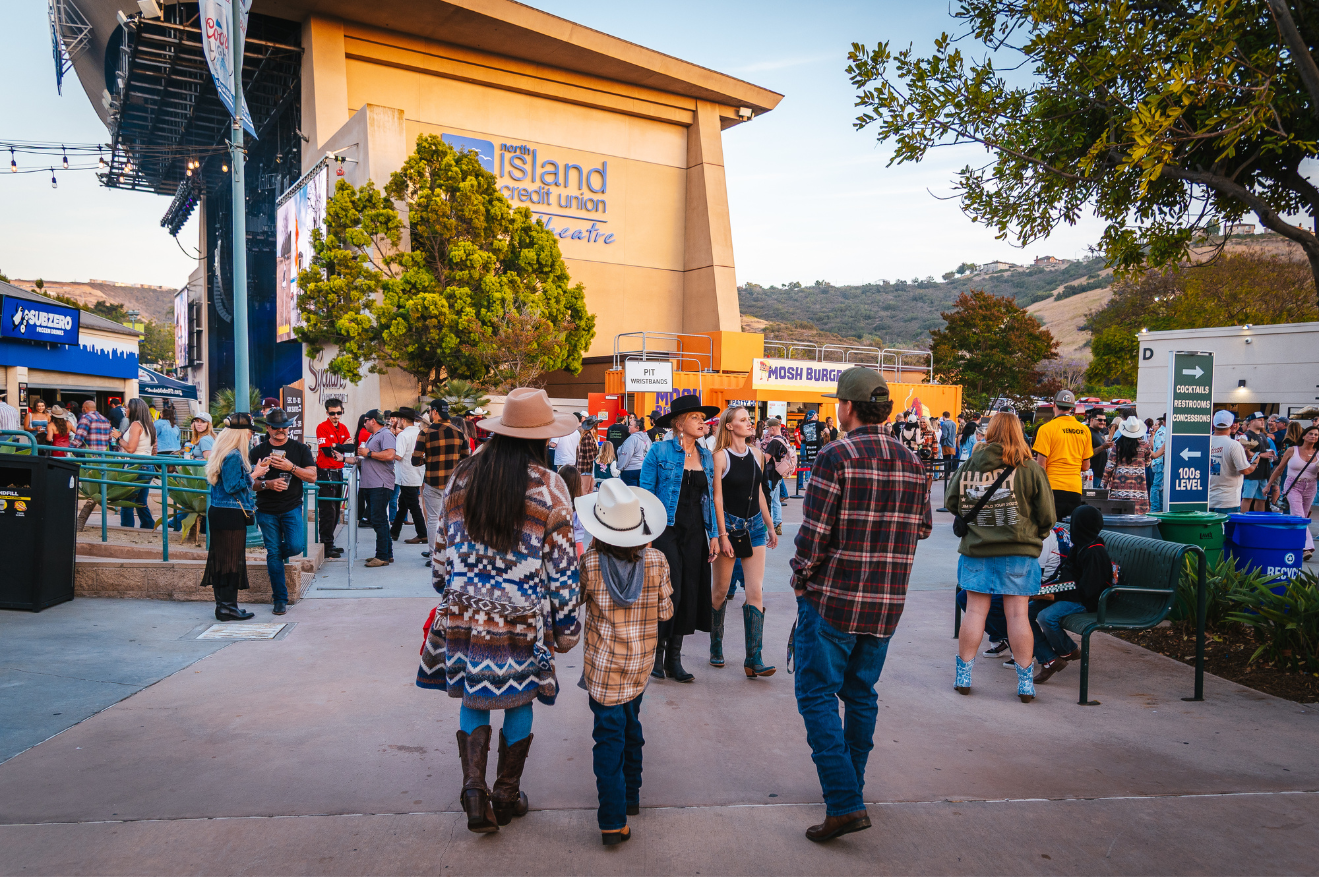 Backshot of family of three walking on West Plaza towards stage before sunset
