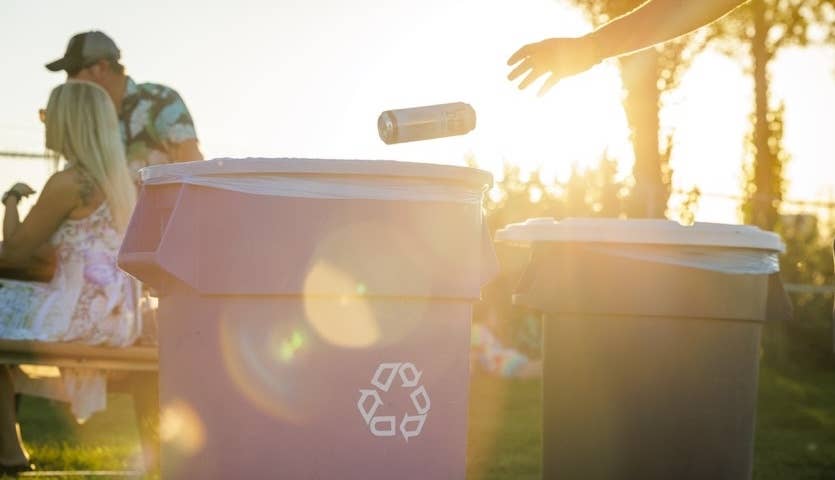 A person tossing a can into a recycling bin