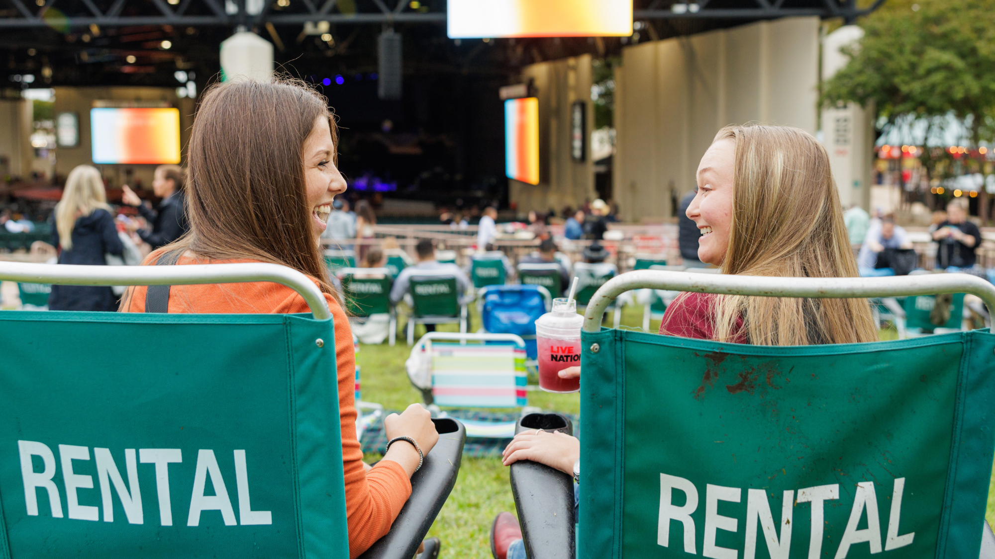 Two girls sit in lawn chairs on the lawn chatting and smiling at each other.