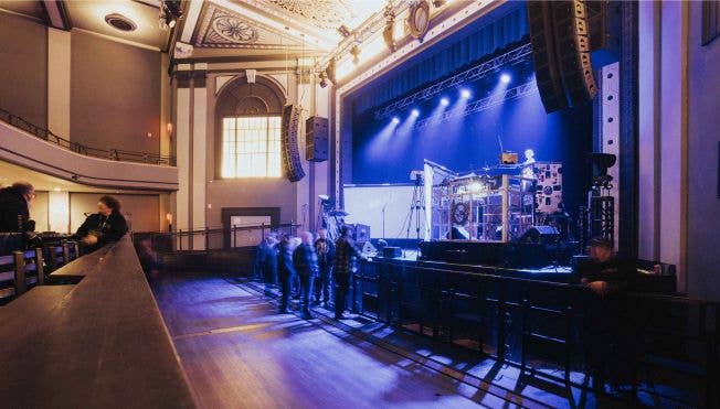 View of fans standing along the barricade facing props and equipment on the stage.