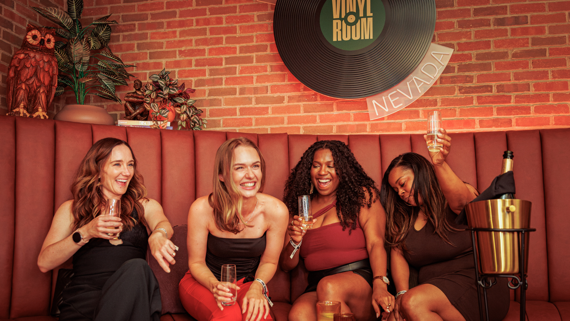 Four girls sit in a VIP booth with champagne bottle service. They are laughing and cheersing.