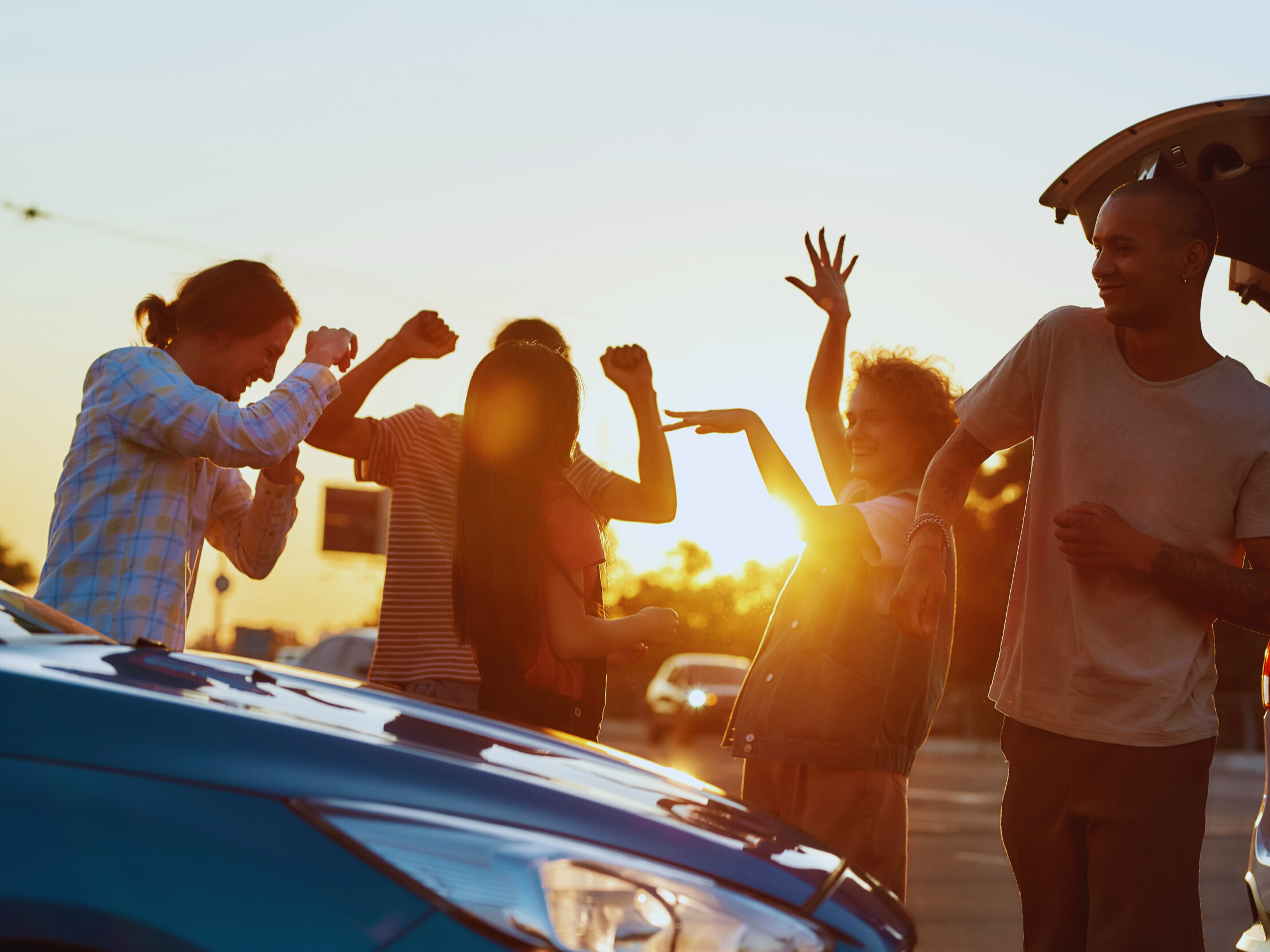 A group of people dancing next to a parked vehicle